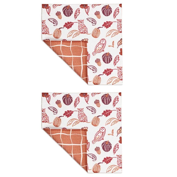 Two folded kitchen towels with a fall harvest pattern, featuring pumpkins, acorns, leaves, and owls in terracotta and brown on a white background, with a terracotta grid pattern visible on the reverse side.