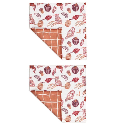 Two folded kitchen towels with a fall harvest pattern, featuring pumpkins, acorns, leaves, and owls in terracotta and brown on a white background, with a terracotta grid pattern visible on the reverse side.
