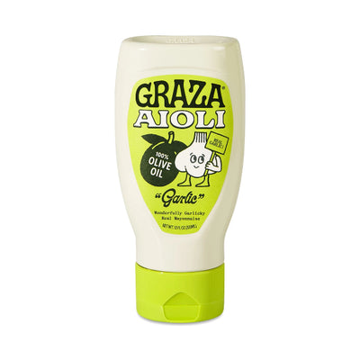 A squeeze bottle of Graza Aioli Garlic Olive Oil dressing on a solid white background. The bottle is off-white with a bright lime green cap and a matching lime green label featuring the brand name and a cartoon garlic character.