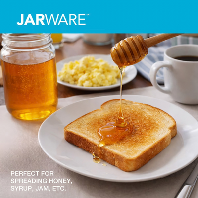 A jar of honey sits on a table beside toast being drizzled with honey from a wooden dipper, with a cup of coffee and a plate of scrambled eggs in the background. The brand name JARWARE appears at the top, and text at the bottom says it is perfect for spreading honey, syrup, jam, etc.