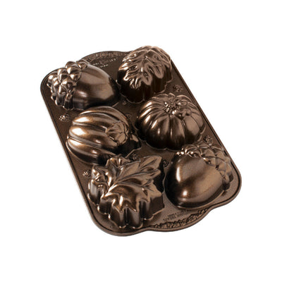 A dark brown cast iron loaf pan with decorative autumn-themed molds shaped like acorns, pumpkins, and leaves, shown on a plain white background.