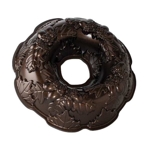 A dark brown bundt cake pan with an embossed holly and grape design, shown on a solid white background.