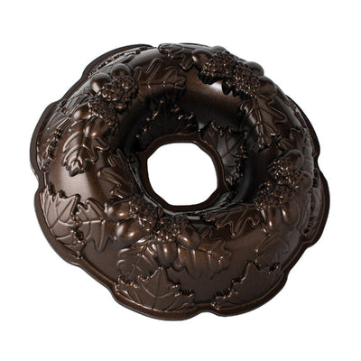 A dark brown bundt cake pan with an embossed holly and grape design, shown on a solid white background.