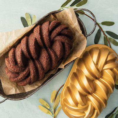 Braided chocolate bread in a loaf pan with a decorative mold on a light green background.