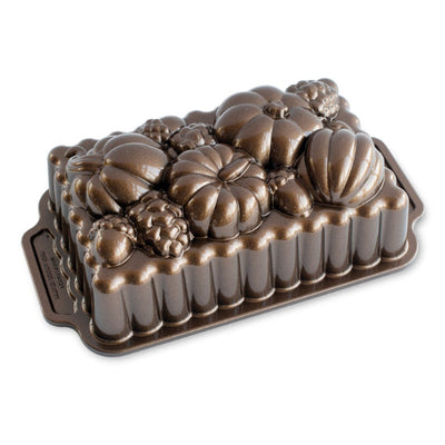 A dark brown cast iron loaf pan with a decorative autumn harvest design featuring pumpkins, a grapevine, and pinecones on top, shown on a plain white background.