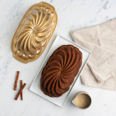 Baked cake with a decorative mold on a marble surface with cinnamon sticks and a towel.