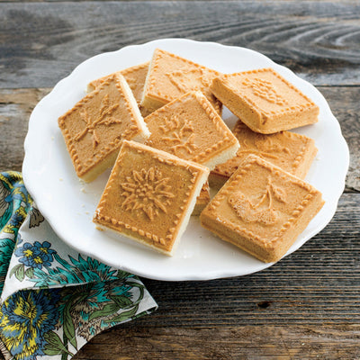 Square cookies with embossed designs on a white plate on a wooden surface